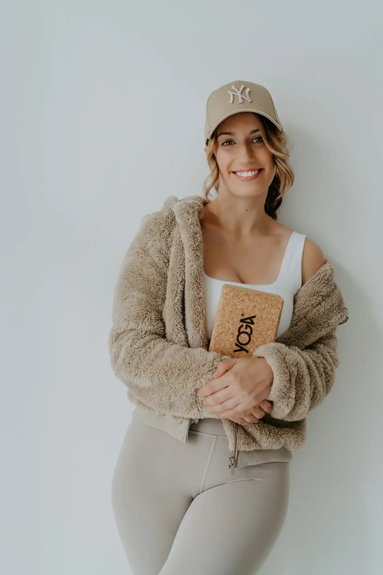Frau in sportlicher Kleidung und Cap lächelt in die Kamera und hält ein Notizbuch, während ein zweites Bild sie bei einer Yoga-Pose zeigt. Modernes Personal Brand Shooting für authentische Business- und Lifestyle-Darstellung.
