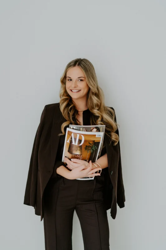 Businessfoto einer Frau im schwarzen Blazer und heller Hose mit geflochtenem Guertel